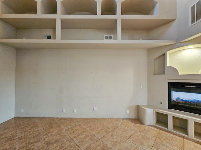 unfurnished living room with tile patterned floors, a multi sided fireplace, and visible vents