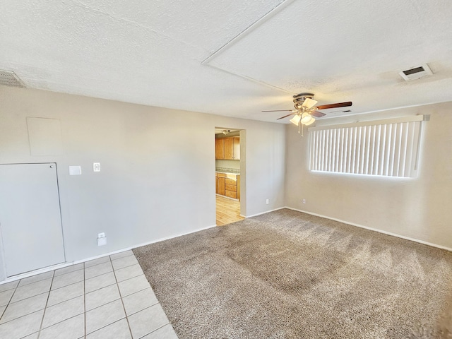 spare room featuring light tile patterned floors, light colored carpet, visible vents, a ceiling fan, and a textured ceiling