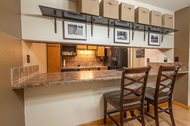 kitchen featuring sink, a kitchen bar, decorative backsplash, black fridge, and light wood-type flooring