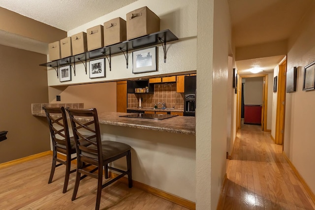 bar featuring black electric cooktop, a textured ceiling, light hardwood / wood-style floors, and decorative backsplash