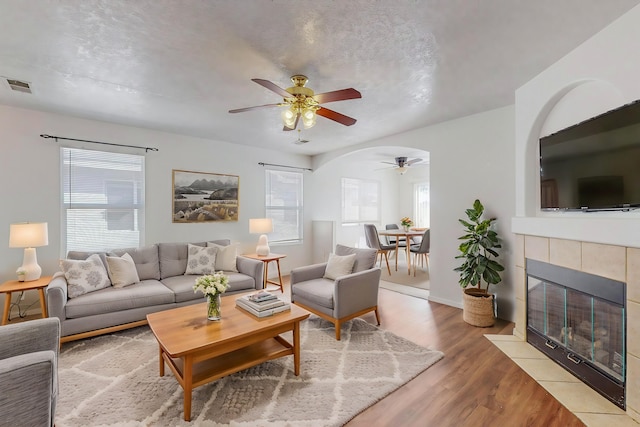 living room featuring a tiled fireplace, light hardwood / wood-style flooring, and ceiling fan