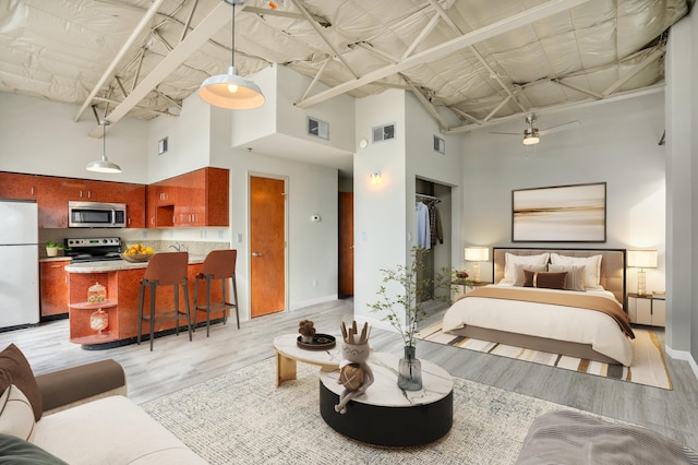 bedroom featuring white fridge, a towering ceiling, and light hardwood / wood-style flooring