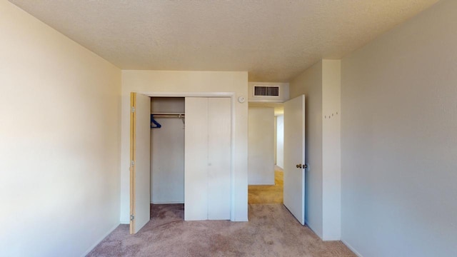 unfurnished bedroom featuring light carpet, a textured ceiling, and a closet