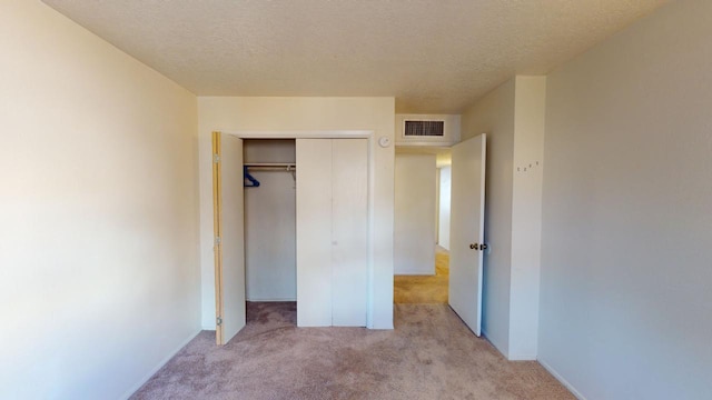 unfurnished bedroom with light colored carpet, a textured ceiling, and a closet