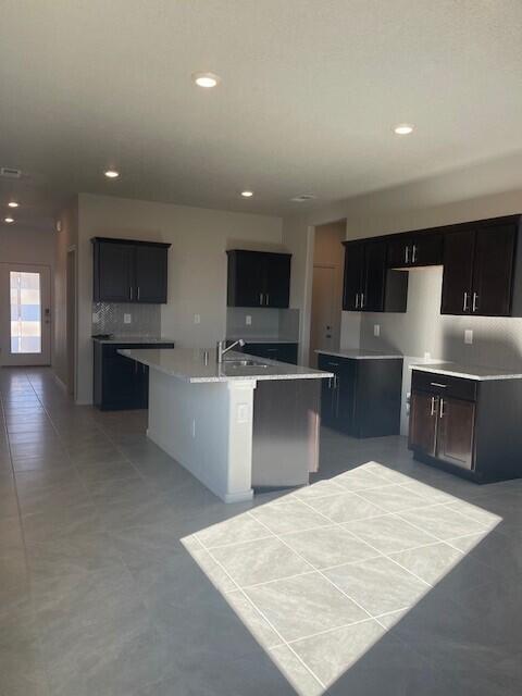 kitchen featuring tile patterned floors, sink, a kitchen island with sink, and backsplash