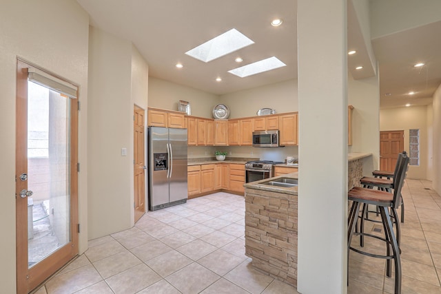 kitchen with light tile patterned flooring, appliances with stainless steel finishes, light brown cabinetry, and a high ceiling