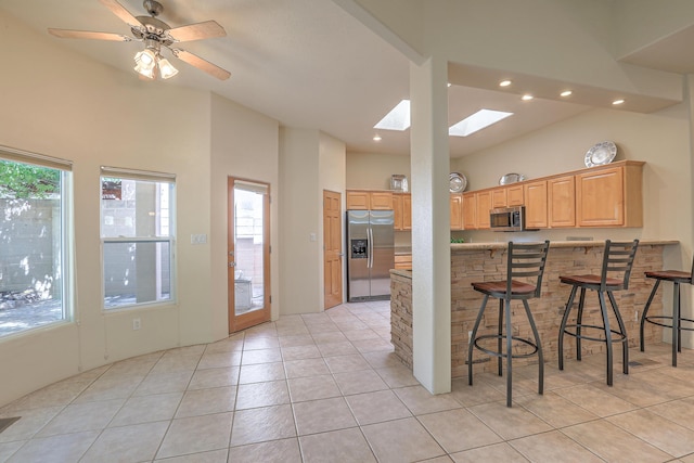 kitchen with light tile patterned flooring, appliances with stainless steel finishes, a breakfast bar, a skylight, and kitchen peninsula