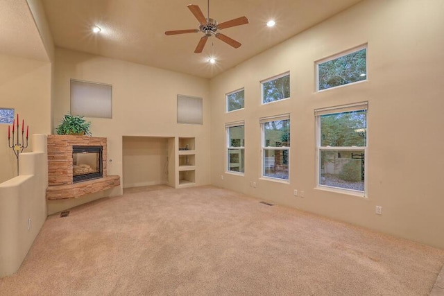 carpeted living room with ceiling fan, a fireplace, and a towering ceiling