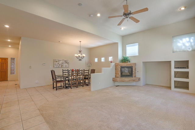 carpeted dining space featuring a stone fireplace and ceiling fan with notable chandelier