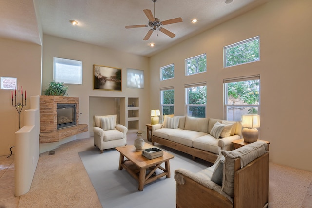 living room featuring ceiling fan, a towering ceiling, light carpet, and a fireplace