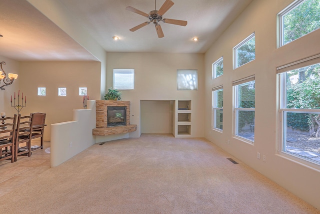 carpeted living room with a stone fireplace, ceiling fan with notable chandelier, and a high ceiling