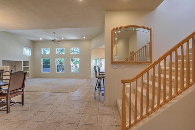 carpeted entryway with ceiling fan and a towering ceiling