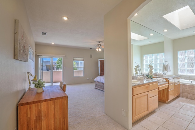 interior space featuring tiled tub, ceiling fan, tile patterned flooring, a skylight, and vanity