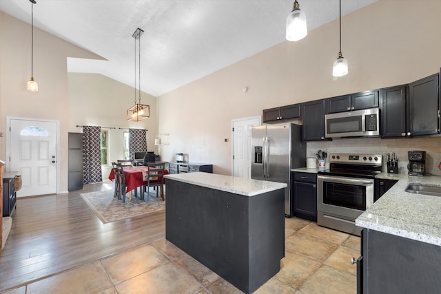 kitchen featuring stainless steel appliances, a kitchen island, light stone countertops, and hanging light fixtures