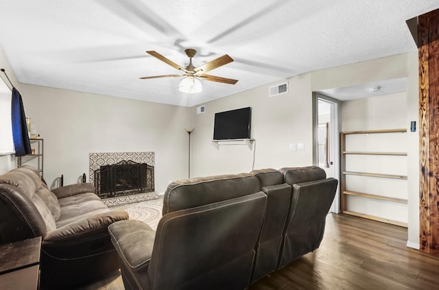 living room featuring ceiling fan, dark hardwood / wood-style floors, a tile fireplace, and a textured ceiling