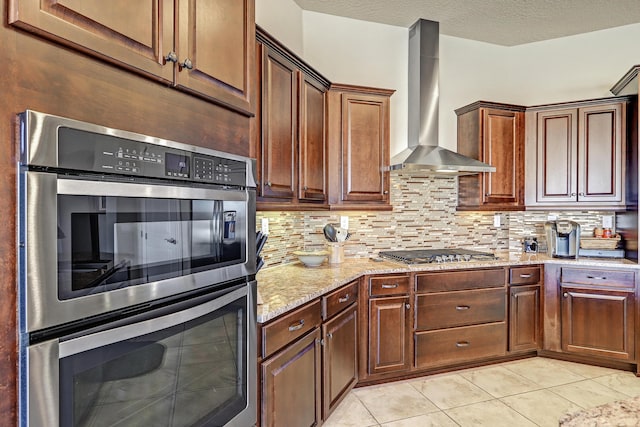 kitchen with light stone counters, wall chimney exhaust hood, stainless steel appliances, and decorative backsplash