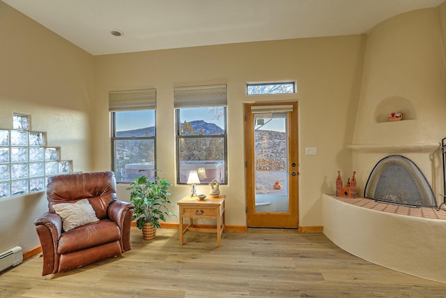 sitting room featuring a baseboard heating unit, a tile fireplace, and light wood-type flooring