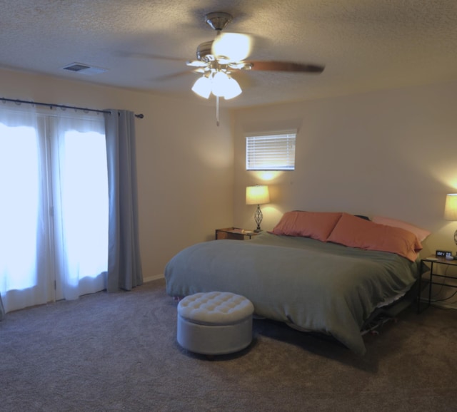 carpeted bedroom featuring ceiling fan, multiple windows, and a textured ceiling