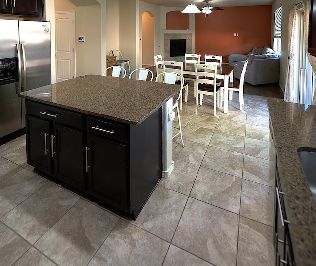 kitchen featuring ceiling fan, a kitchen breakfast bar, a center island, stainless steel refrigerator with ice dispenser, and a tiled fireplace