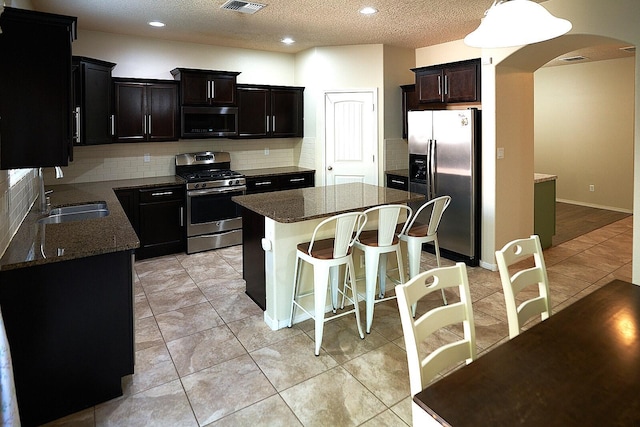 kitchen featuring a kitchen island, sink, decorative backsplash, light tile patterned floors, and stainless steel appliances