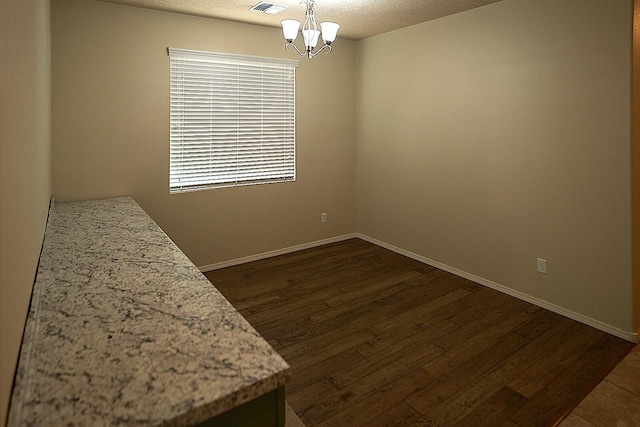 empty room featuring dark wood-type flooring, a notable chandelier, and a textured ceiling