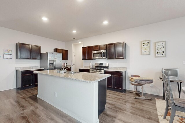 kitchen with sink, hardwood / wood-style floors, stainless steel appliances, dark brown cabinetry, and a center island with sink