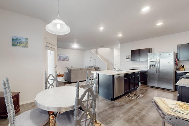 kitchen featuring sink, light hardwood / wood-style flooring, appliances with stainless steel finishes, an island with sink, and decorative light fixtures