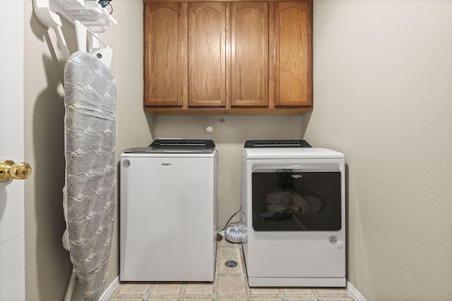 clothes washing area with separate washer and dryer and cabinets