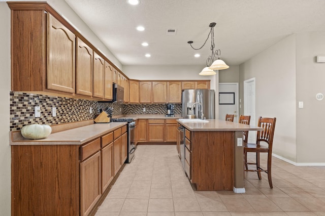 kitchen with tasteful backsplash, light tile patterned floors, pendant lighting, stainless steel appliances, and a kitchen island with sink