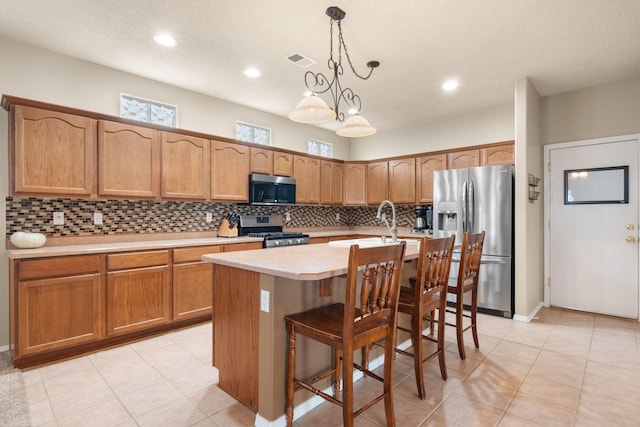 kitchen with a breakfast bar, appliances with stainless steel finishes, hanging light fixtures, an island with sink, and decorative backsplash