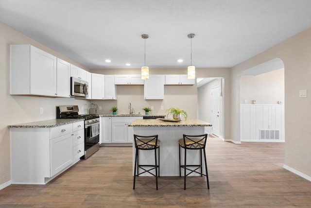 kitchen with a breakfast bar, stone counters, white cabinetry, stainless steel appliances, and a center island