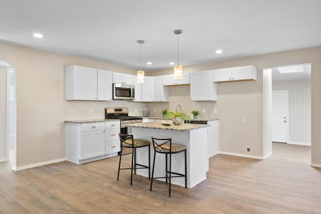 kitchen featuring appliances with stainless steel finishes, hanging light fixtures, light stone countertops, white cabinets, and a kitchen island