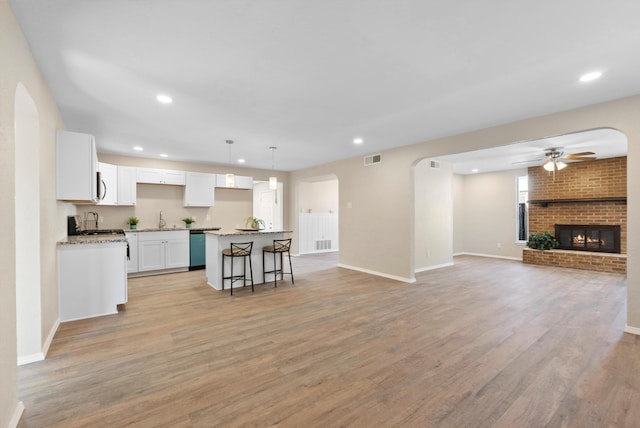 kitchen with sink, white cabinets, a kitchen island, a brick fireplace, and light wood-type flooring