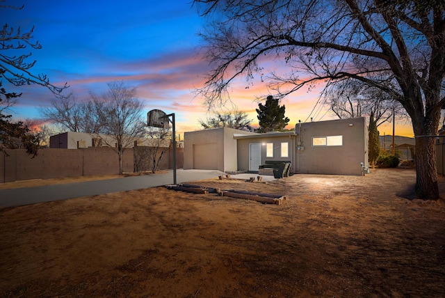 rear view of house featuring fence, driveway, an attached garage, and stucco siding