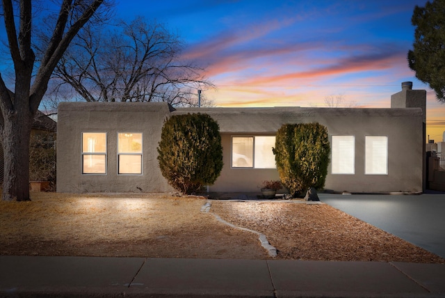 pueblo revival-style home featuring a chimney and stucco siding