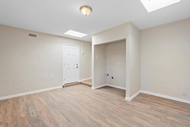 unfurnished room featuring a skylight and light hardwood / wood-style floors