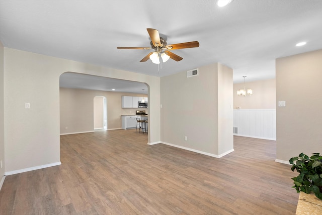 unfurnished living room featuring ceiling fan with notable chandelier and light hardwood / wood-style flooring