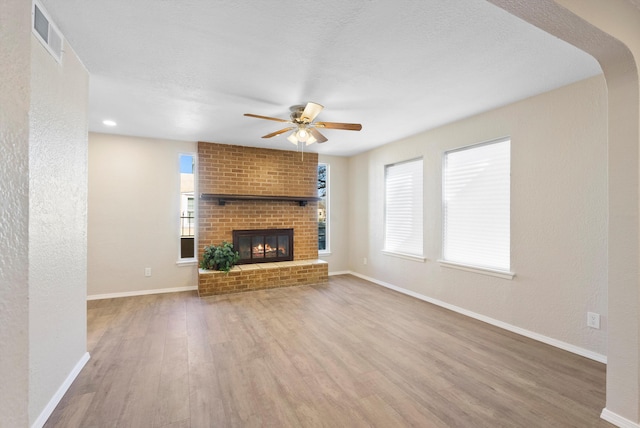 unfurnished living room with a brick fireplace, wood-type flooring, and ceiling fan