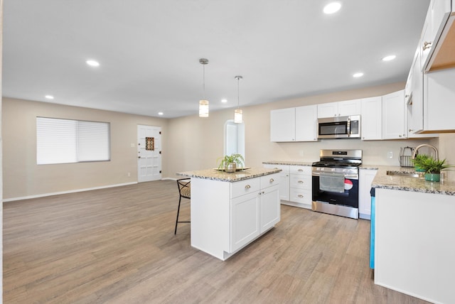 kitchen with sink, appliances with stainless steel finishes, white cabinetry, hanging light fixtures, and a center island