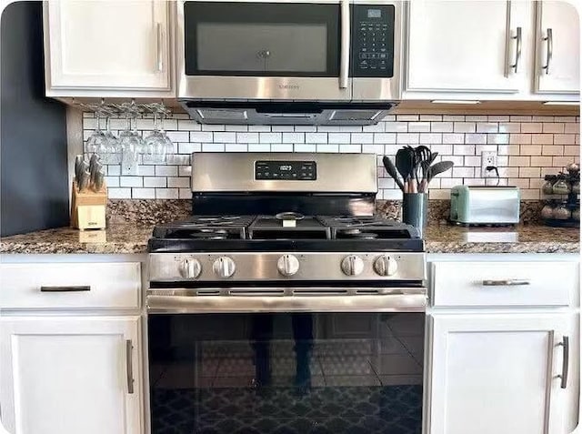 kitchen featuring white cabinetry, appliances with stainless steel finishes, backsplash, and dark stone countertops