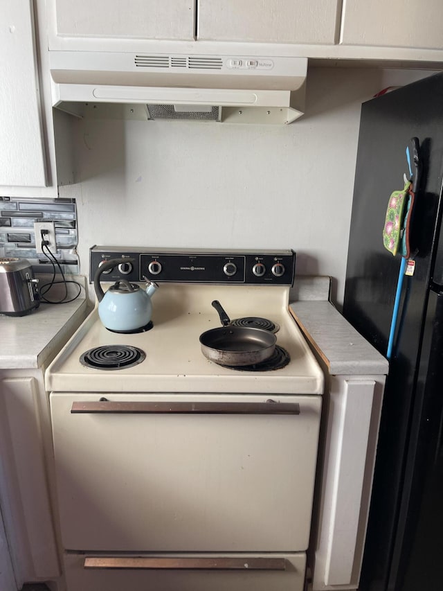 room details with electric stove, black fridge, and white cabinets