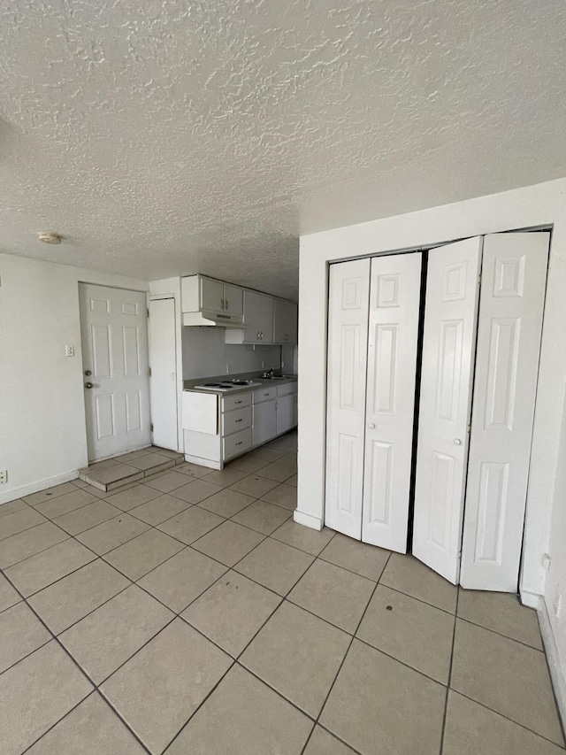 kitchen with sink, light tile patterned floors, white stovetop, white cabinets, and a textured ceiling