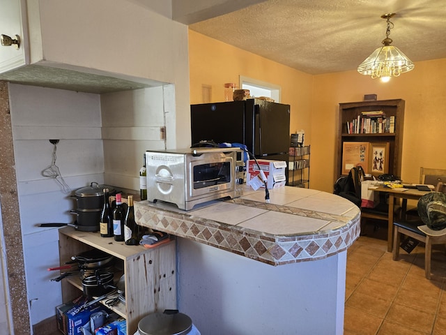 kitchen featuring black fridge, light tile patterned flooring, a textured ceiling, and pendant lighting