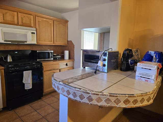 kitchen with black range with gas stovetop, tile counters, kitchen peninsula, and light tile patterned floors