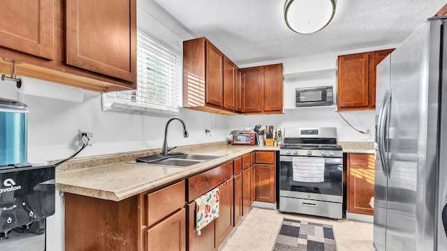 kitchen with appliances with stainless steel finishes, light tile patterned floors, sink, and a textured ceiling