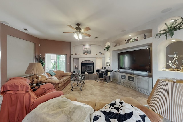 living room with a tile fireplace and ceiling fan