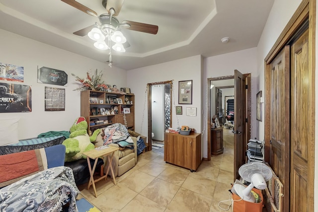 living area featuring a raised ceiling, ceiling fan, and light tile patterned flooring