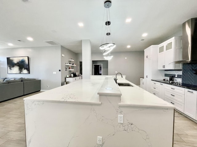 kitchen with pendant lighting, a large island, sink, and wall chimney range hood