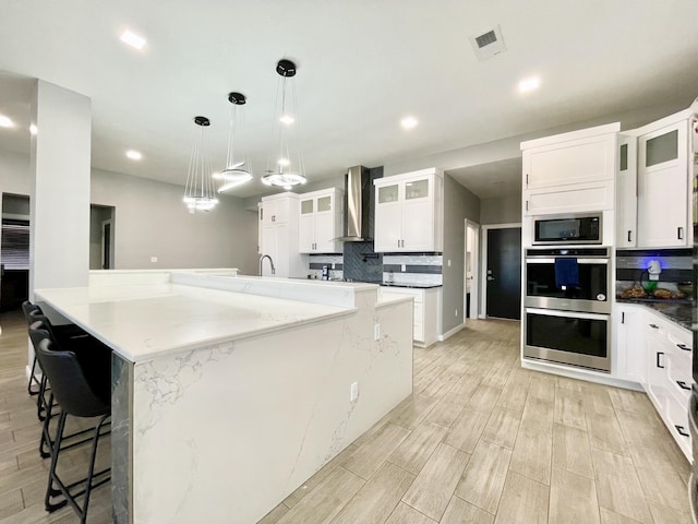 kitchen with pendant lighting, wall chimney exhaust hood, a kitchen breakfast bar, and white cabinets