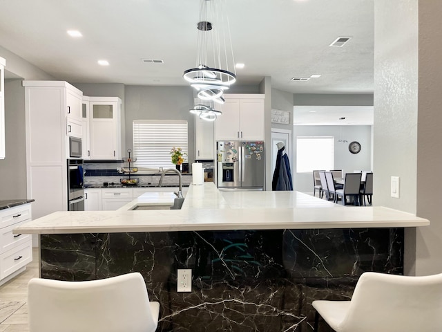 kitchen with sink, a breakfast bar, appliances with stainless steel finishes, white cabinets, and decorative light fixtures